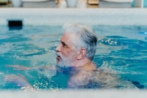 A senior man with grey hair swimming in a pool, enjoying leisure and relaxation.